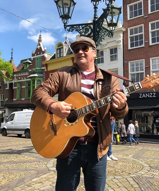 Potret sang pemandu dengan gitar di sebuah alun-alun Alkmaar, fasad kota di belakangnya